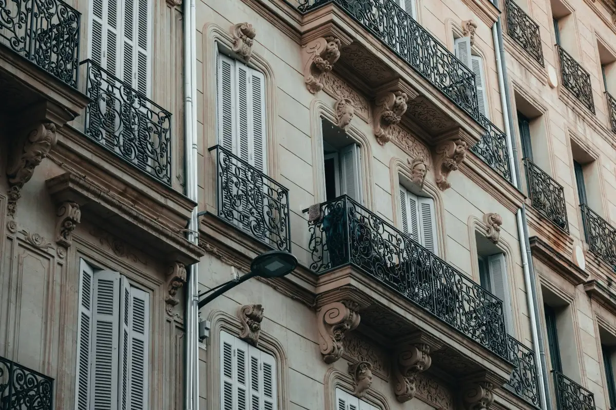 La façade d’un immeuble haussmannien, ses balcons en fer forgé et ses volets