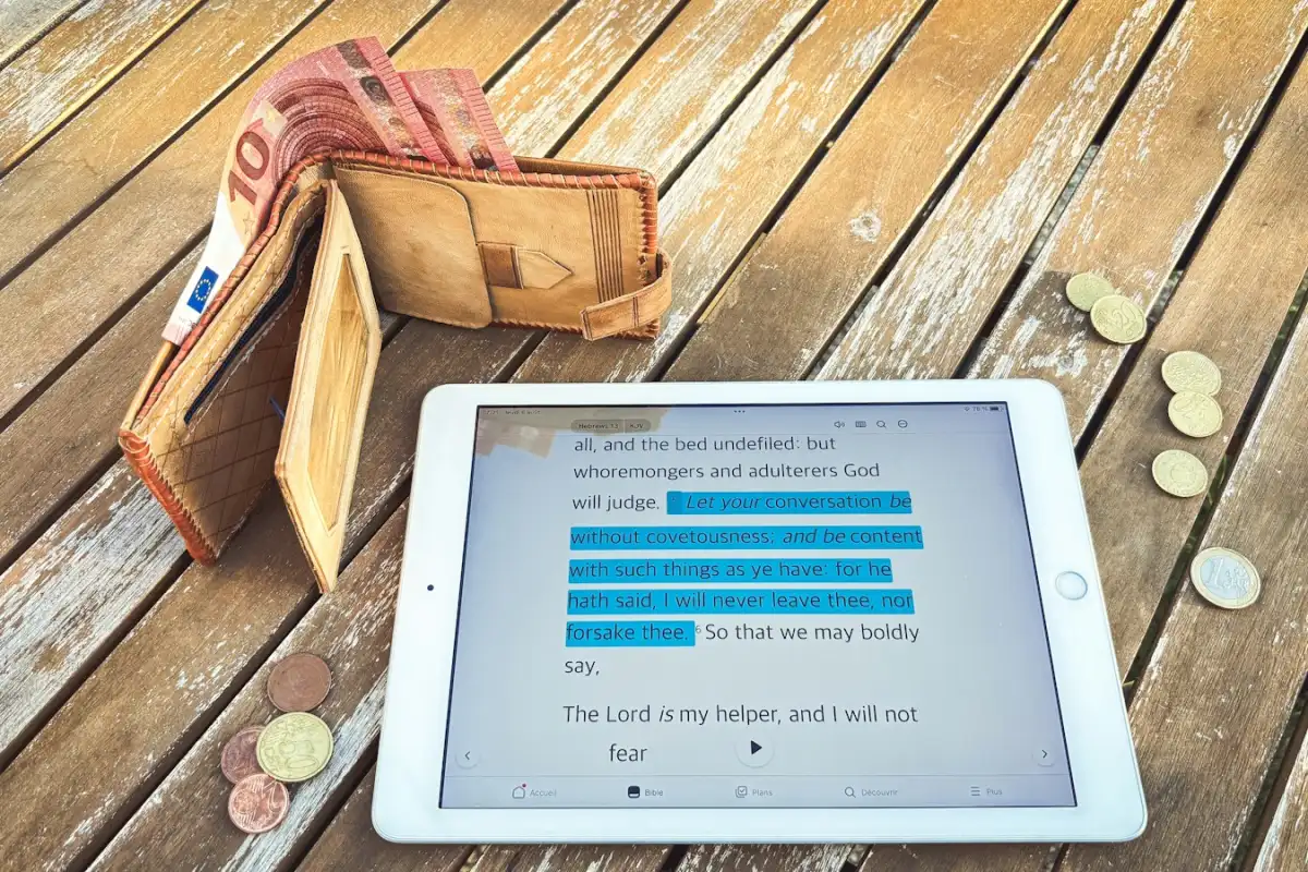 Un portefeuille ouvert rempli de billets en euros, à côté d’une tablette affichant des graphiques financiers et de quelques pièces, sur une table en bois
