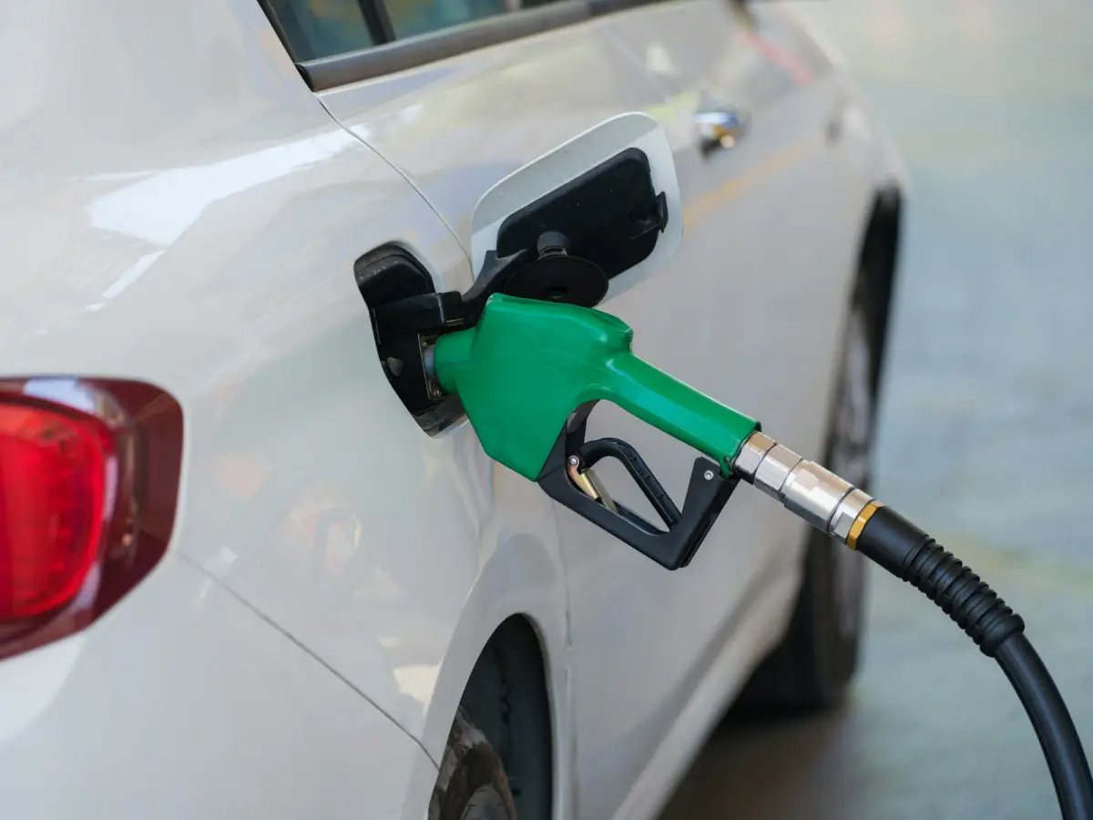 Un pistolet à carburant vert engagé dans le réservoir d’une voiture blanche, dans une station-service