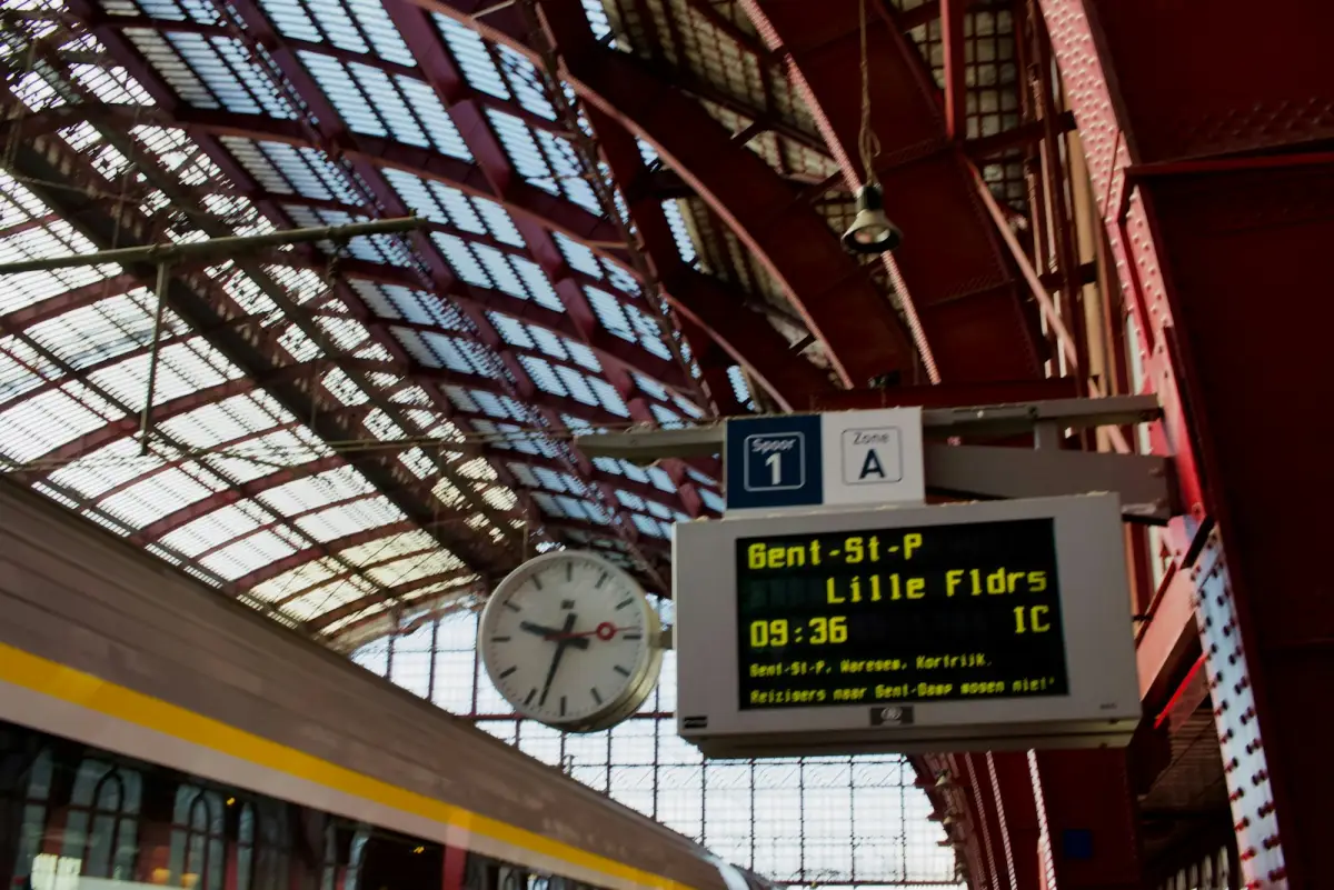 Le quai d’une gare sous une verrière à arcs rouges, avec une horloge et un panneau lumineux annonçant un train pour Lille Flandres à 9 h 36