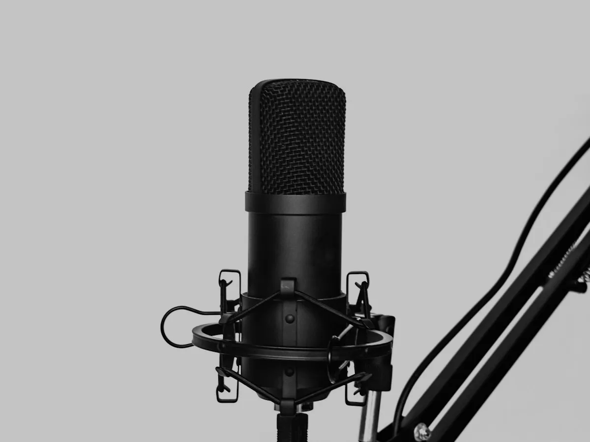 Un micro de studio noir dans sa suspension antichoc, fixé à un bras articulé, sur un fond gris clair