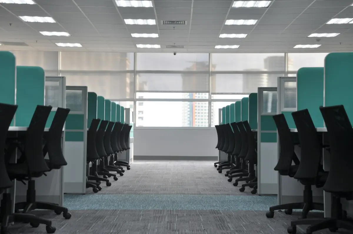 Des rangées de chaises de bureau vides devant les cloisons d’un open space désert