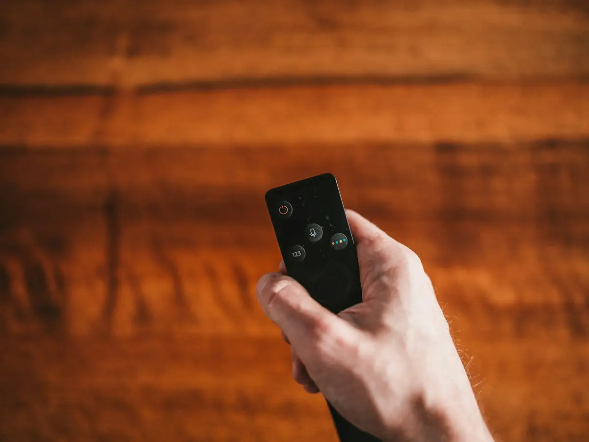Une main tenant une télécommande de télévision au-dessus d’une table en bois