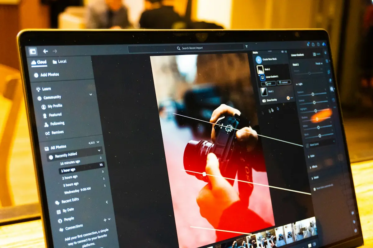 L’écran d’un ordinateur portable ouvert sur un logiciel de retouche photo, avec la photo d’une main tenant un appareil photo, des curseurs de réglage et des repères de dégradé