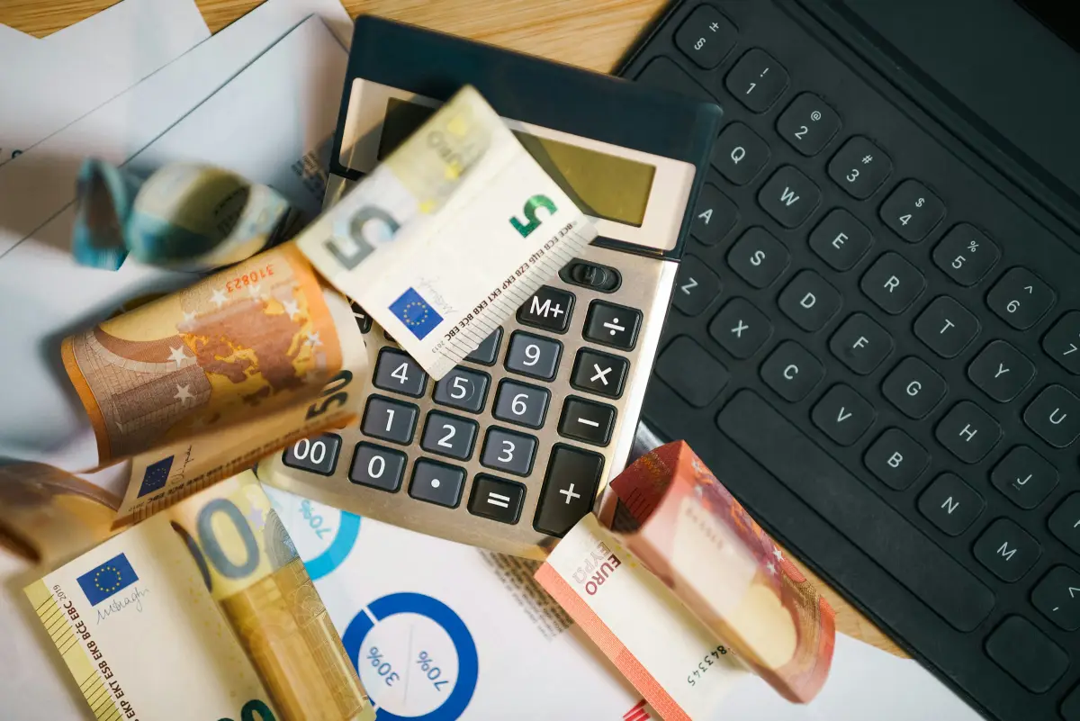 Des billets en euros et une calculatrice posés sur des documents chiffrés, à côté d’un clavier