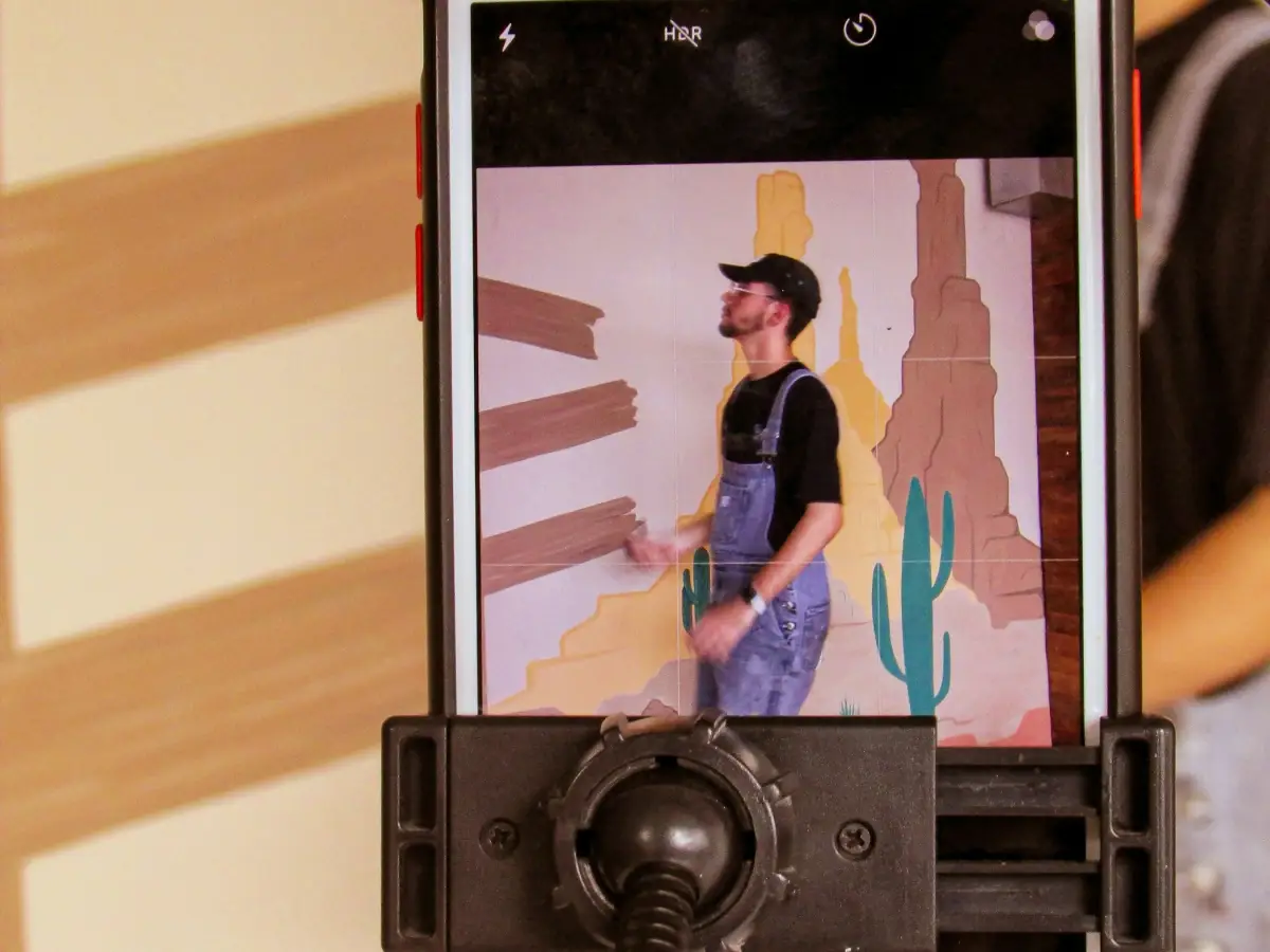 Un téléphone monté sur un support filme en cadrage vertical une personne qui peint une fresque